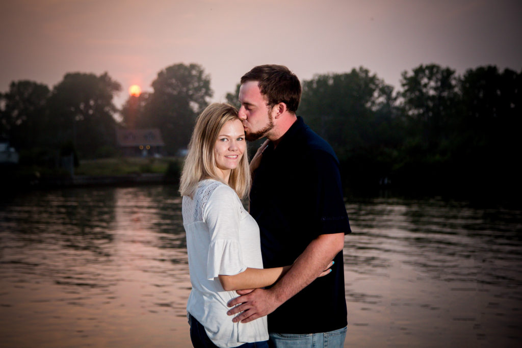 man kisses his fiance on the temple with the sunset in the background during port burwell engagement photography by london ontario photographer Woodgate Photography