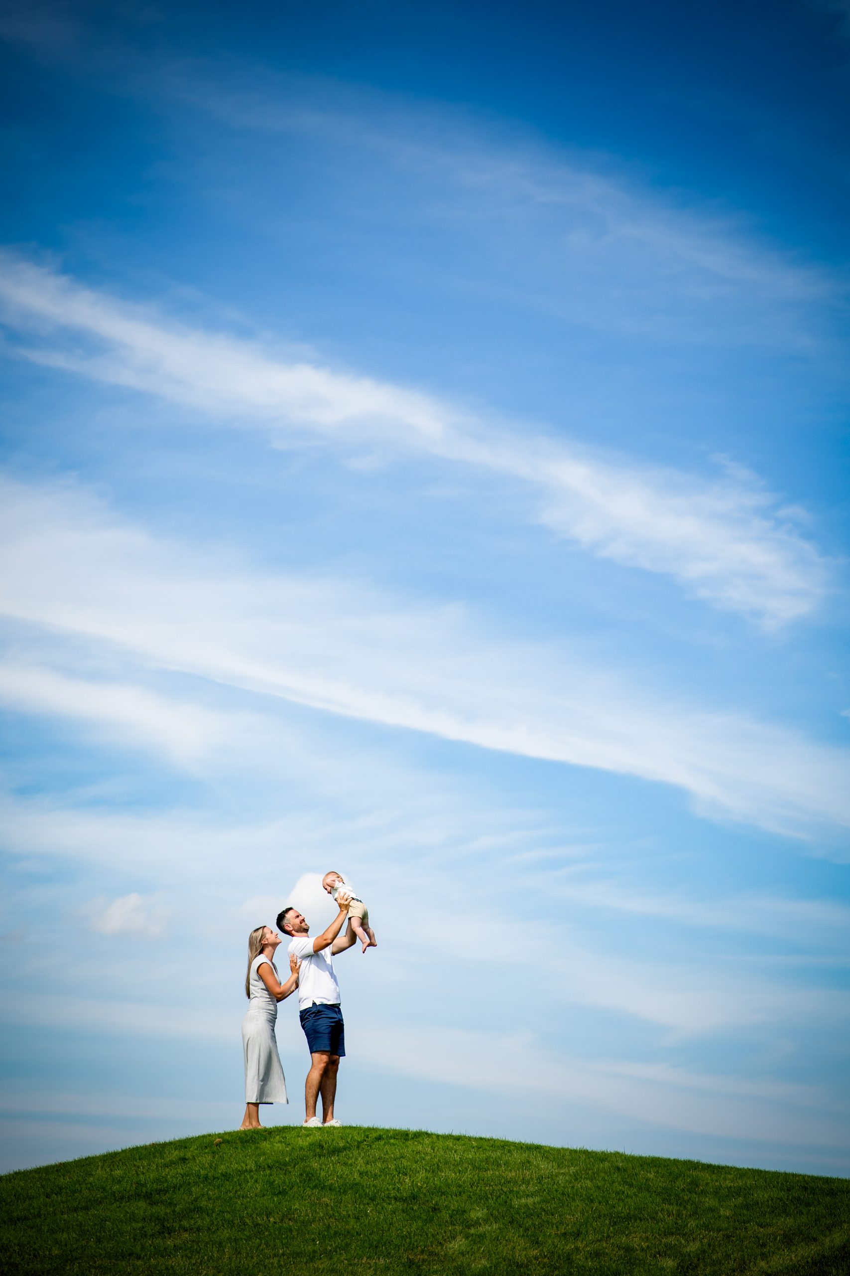 family photography london ontario standing on hill at westhaven golf course holding baby in the air and lots of blue sky