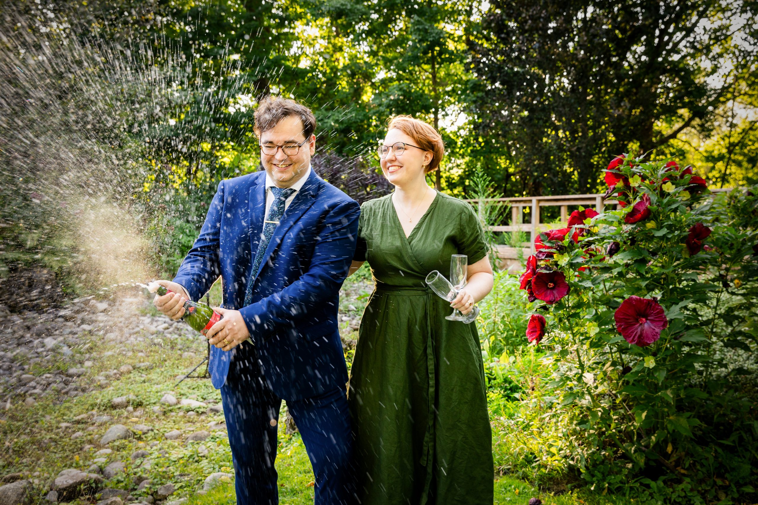 couple spray champagne at civic gardens with red flowers Engagement Photography London Ontario