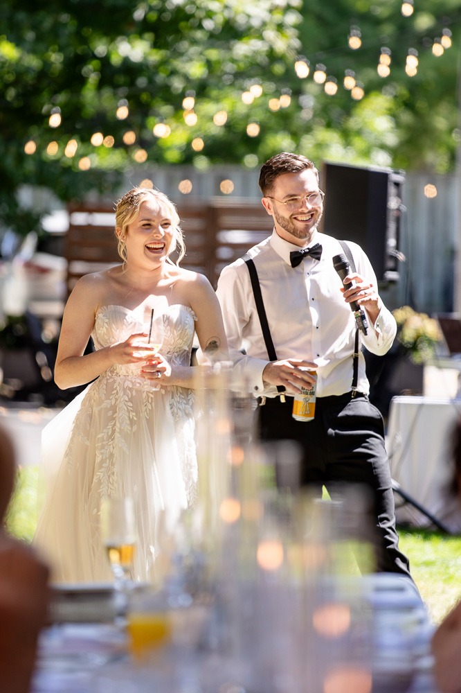 couple smile candidly during speeches at outdoor wedding