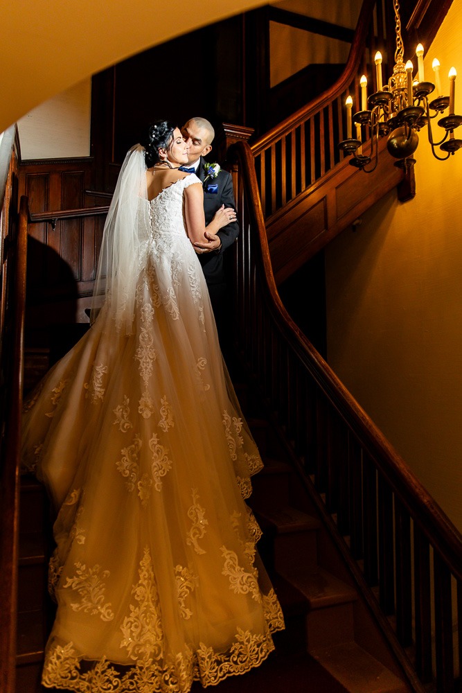 Couple kiss with full wedding gown visible dramatically lit on stairs wedding photography london ontario